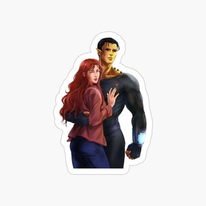 May include: A woman with long red hair is standing next to a man with green skin. The man is wearing a black suit with a blue and white device on his wrist. The woman is wearing a red shirt and blue jeans. They are both looking at the camera.