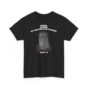 Könnte beinhalten: Schwarzes T-Shirt mit einem weißen Aufdruck eines Männergesichts mit Bart und dem Text "PAPA ZU SEIN IST GAR NICHT SO STRESSIG. MARC. 29"