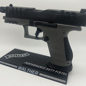 Puede incluir: Una pistola Walther Performance Duty de color negro y gris en un expositor negro con el logotipo de Walther y las palabras "Performance Duty Pistol".
