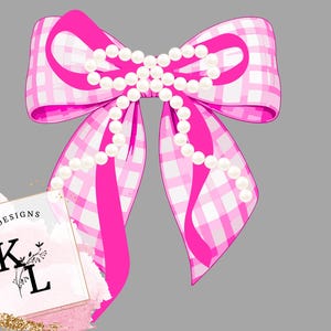 Puede incluir: Un lazo rosa brillante con un patr&oacute;n de cuadros blancos y una hilera de perlas blancas. El lazo tiene colas largas y fluidas y est&aacute; sobre un fondo gris. La imagen tambi&eacute;n incluye un logotipo que dice "CREATIVE DESIGNS" con las letras "K L".