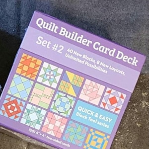 Puede incluir: Caja morada con el texto "Quilt Builder Card Deck Set #2" y "40 New Blocks, 8 New Layouts, Unlimited Possibilities". La caja muestra una variedad de diseños de bloques de colcha coloridos. El texto "QUICK & EASY Block Tool series" y "(50) 4"x4" two-sided cards" también es visible.