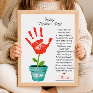 Puede incluir: Un cuadro enmarcado para el Día de la Madre con una flor roja hecha con huella de mano, hojas verdes y una maceta turquesa. La impresión incluye el texto "Happy Mother's Day!" y un poema. El año "2026" está en la maceta y el nombre "Olivia" está en la parte inferior.