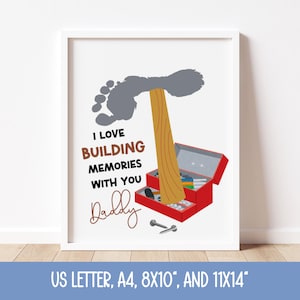 Könnte beinhalten: Ein gerahmter Druck mit weißem Rand zeigt einen grauen Fußabdruck, einen Holzbalken und eine rote Werkzeugkiste. Der Text lautet "I LOVE BUILDING MEMORIES WITH YOU Daddy". Der Druck ist in den Größen US Letter, A4, 20.32cm x 25.4cm und 27.94cm x 35.56cm erhältlich.