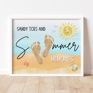 May include: A framed print with a beach theme. The artwork features the text "Sandy Toes and Summer Memories" with a smiling sun, footprints, a crab, and a beach ball. The background has a blue ocean and sandy beach.
