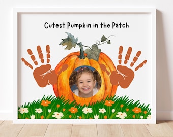 May include: A framed print featuring a smiling child's photo within an orange pumpkin illustration. The pumpkin is surrounded by handprints and sits above a grassy field with flowers. The text "Cutest Pumpkin in the Patch" is at the top.
