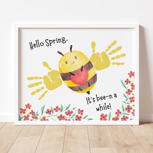 May include: A framed print with a whimsical bee design. The bee is yellow and brown with a red heart and handprint wings. Text reads "Hello Spring" and "It's bee-n a while!" Floral accents frame the bottom.