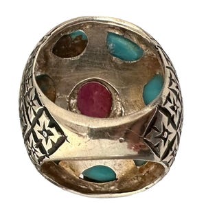 May include: A silver ring with a detailed floral design and five gemstones. The ring features a large, oval-shaped red gemstone surrounded by four smaller turquoise gemstones.