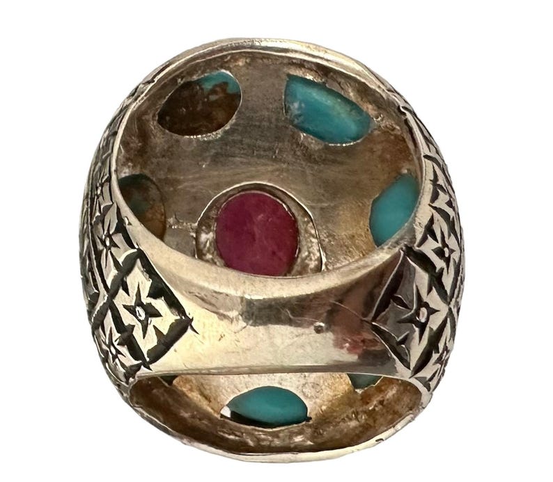 May include: A silver ring with a detailed floral design and five gemstones. The ring features a large, oval-shaped red gemstone surrounded by four smaller turquoise gemstones.