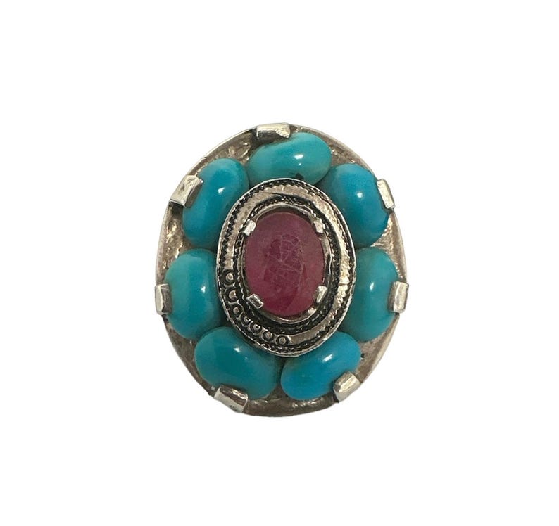 May include: A silver ring with a pink stone surrounded by turquoise stones.