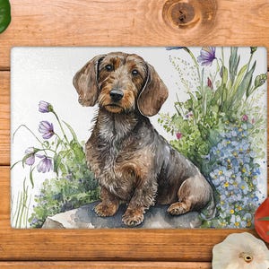 May include: Rectangular chopping board with a watercolour illustration of a brown and grey dachshund dog amidst purple and blue flowers. The dog has long ears and a focused gaze. The background is white.