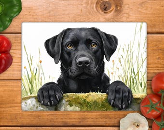 Könnte beinhalten: Ein rechteckiges Glasschneidebrett mit einer detaillierten Illustration eines schwarzen Labrador Retrievers mit bernsteinfarbenen Augen, der seine Vorderpfoten auf einen moosigen Steinrand in hohem Gras vor weißem Hintergrund stützt.