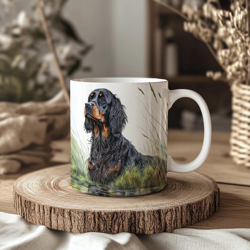 K&ouml;nnte beinhalten: Wei&szlig;e Keramiktasse mit einer detaillierten Illustration eines schwarz-lohfarbenen Gordon Setter-Hundes in einem grasbewachsenen Feld. Der Hund wird mit konzentriertem Blick dargestellt, umgeben von gr&uuml;nem und beigem Laub. Die Tasse steht auf einem Holzuntersetzer.