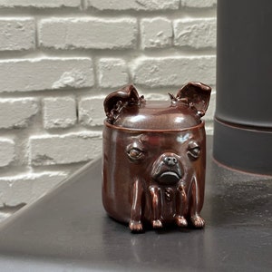 Może przedstawiać: Brązowy ceramiczny dzbanek w kształcie chihuahua z błyszczącym wykończeniem. Dzbanek ma pokrywkę i cztery nóżki.