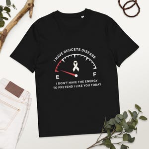 May include: Black t-shirt with the text "I HAVE BEHCETS DISEASE" and "I DON'T HAVE THE ENERGY TO PRETEND I LIKE YOU TODAY". The design includes a gauge with a ribbon symbol. A casual tee for awareness.