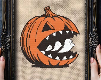 Może przedstawiać: Oprawiony haft krzyżykowy o tematyce Halloween. Przedstawia pomarańczową dynię z poszarpaną paszczą, odsłaniającą trzy białe duszki. Czarna rama ma ozdobne detale, na tle teksturowanym.