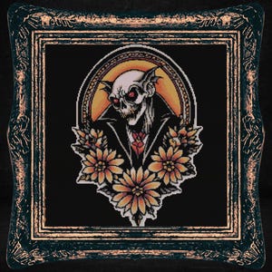 May include: A framed cross-stitch embroidery featuring a vampire with red eyes and fangs, wearing a black coat and surrounded by yellow flowers.