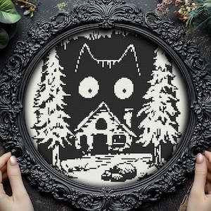 May include: Black and white cross-stitch embroidery of a cat's face with large eyes, a small house, and two pine trees. The embroidery is framed in a black ornate frame.