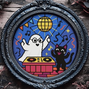 Könnte beinhalten: Eine kreisrunde Stickerei in einem schwarzen Rahmen, die ein Gespenst und eine schwarze Katze mit einer Discokugel im Hintergrund zeigt. Das Gespenst und die Katze tragen beide Partyhüte und heben ihre Hände in die Luft. Die Stickerei ist auf einem blauen Hintergrund mit bunten Akzenten.