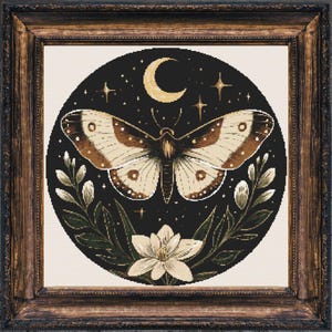 Puede incluir: Obra de arte enmarcada con un diseño de polilla. La polilla tiene alas marrones y beige, sobre un fondo negro con una luna creciente, estrellas y elementos florales. El marco es de madera oscura.