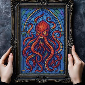 May include: Framed artwork featuring a stained-glass style design of a red octopus with a menacing expression. The octopus is set against a blue background with an arched top. The frame is black with ornate detailing.