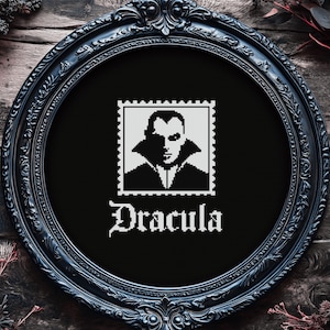 May include: Black and white embroidery of a vampire in a black cape with the word "Dracula" underneath in a gothic font. The embroidery is framed in a black ornate frame.
