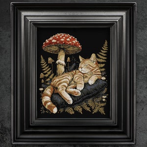 Op de afbeelding: Een bruin-witte tabbykat slaapt op een blauw kussen onder een rode en witte paddenstoel in een bosrijke omgeving.