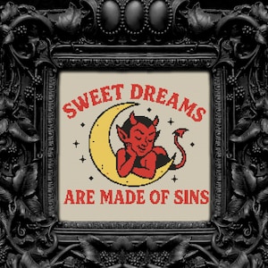 May include: Cross-stitch art in a black ornate frame. The artwork features a red devil resting on a yellow crescent moon, with the text "SWEET DREAMS ARE MADE OF SINS" in red. The background is a neutral beige.