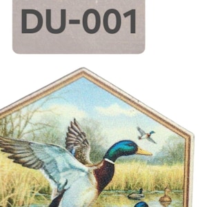 May include: A hexagonal wooden coaster with a colorful image of ducks on a lake. The coaster has a gold border and the text "DU-001" is printed on a gray label above the coaster.