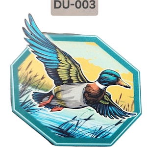 Può includere: Un adesivo ottagonale color turchese con un'illustrazione colorata di un'anatra che vola sopra un specchio d'acqua. L'adesivo ha il testo "DU-003".