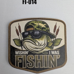 May include: A patch featuring a cartoon bass wearing sunglasses and a camouflage hat. The text "Wishin' I Was Fishin'" is displayed below the fish. The patch has a brown border and cattails on either side of the fish.