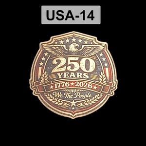 以下が含まれることがあります： 上部に「USA-14」の文字が入った木製の記念エンブレム。エンブレムは、ワシ、星、そして「250 YEARS 1776-2026 We The People」の文字を盾の形にしています。エンブレムは茶色と赤色です。