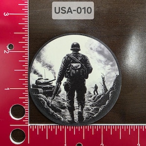 May include: Black and white illustration of a soldier walking through a battlefield with a tank in the background. The image is circular and has the text "USA-010" at the top.