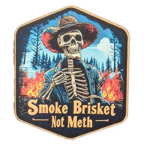 Può includere: Spilla esagonale in legno con uno scheletro con cappello da cowboy e giacca, davanti a una foresta e fiamme. Il testo dorato recita "Smoke Brisket Not Meth".