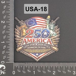 Könnte beinhalten: Ein Gedenkemblem zum 250-jährigen Jubiläum Amerikas mit der amerikanischen Flagge, der Freiheitsstatue und dem Text "250 AMERICA 1776-2026 Celebrating 250 Years". Das Emblem enthält Bilder von Kanonen und Kugeln.