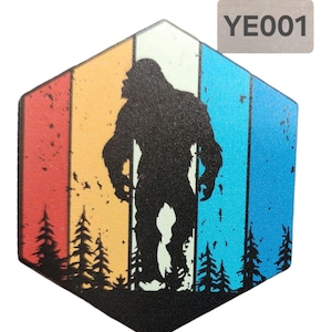 May include: A hexagonal shaped coaster with a retro-style design featuring a silhouette of Bigfoot standing in a forest. The background is a colorful gradient of red, orange, yellow, green, blue, and purple.