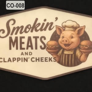 May include: A rectangular sticker with rounded corners featuring the text Smokin' MEATS AND CLAPPIN' CHEEKS in brown font. To the right, a cartoon pig wearing a chef hat and apron holds two hamburgers. The code CO-008 is printed in the top left corner.