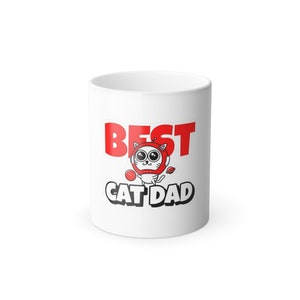 Puede incluir: Taza de cerámica blanca con las palabras "BEST CAT DAD" en rojo y negro. La taza presenta un gato de dibujos animados con un casco rojo y una bola roja.