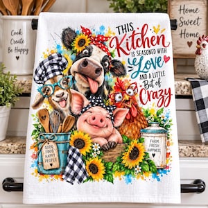 May include: A white kitchen towel featuring a colorful illustration of a cow, goat, pig, and chicken wearing accessories. The text reads: This Kitchen is seasoned with Love and a little Bit of Crazy. A blue bucket with wooden utensils is included.