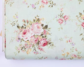 May include: A roll of floral fabric featuring a repeating pattern of pink roses, smaller pink and yellow flowers, and green leaves on a pale green background. The fabric is tightly rolled, showing the edge of the material.