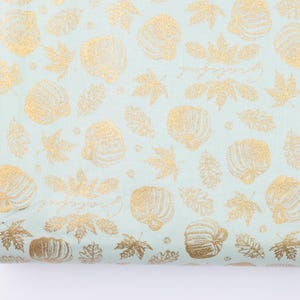 May include: A light blue fabric with a gold foil print of pumpkins and leaves. The fabric has a subtle glitter finish.