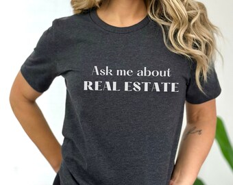 May include: A dark gray t-shirt with the text "Ask me about REAL ESTATE" printed in white.