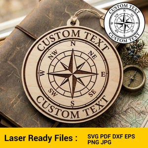 May include: A circular wooden ornament featuring a compass design and the words "CUSTOM TEXT" engraved around the edge. The compass rose has directional indicators. The ornament is suspended by a string. The text "Laser Ready Files" is at the bottom.