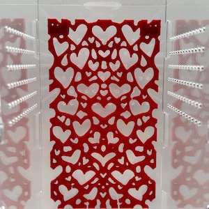 May include: A clear plastic box with a red heart-shaped design on the inside. The design is made of a thin, flexible material and is visible through the clear plastic.