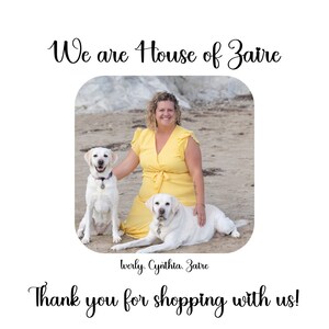 May include: A woman in a yellow dress sits on a sandy beach with two white Labrador Retrievers. The text "We are House of Zaire" is at the top of the image and the text "werly. Cynthia. Zaire" is at the bottom of the image. The text "Thank you for shopping with us!" is at the bottom of the image.