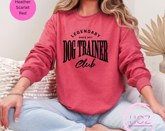 Puede incluir: Sudadera roja escarlata jaspeada con el texto negro "LEGENDARY DOG TRAINER CLUB SINCE 2011". La sudadera es de cuello redondo y está hecha de un material suave. La imagen también incluye un círculo rosa con el texto "Heather Scarlet Red".