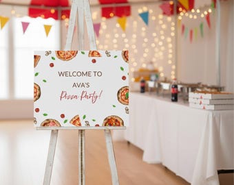 May include: A white wooden easel displays a sign that reads "Welcome to Ava's Pizza Party!" in red script. The sign is decorated with pizza illustrations, basil leaves, and tomatoes. The background shows a party setting with a red and white striped tent.