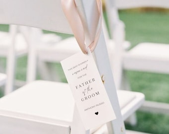 May include: White card with black text that reads "This seat is kindly reserved for the Father of the Groom Anthony Russo" with a small black heart at the bottom.