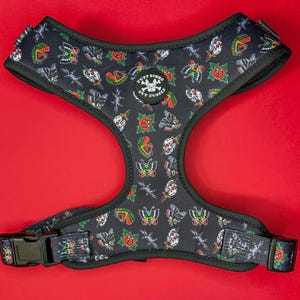 May include: Black dog harness with a tattoo-inspired print featuring butterflies, roses, daggers, and skulls. The harness has a black adjustable buckle and the text "PUFF BONES PET SUPPLY" in a circle.