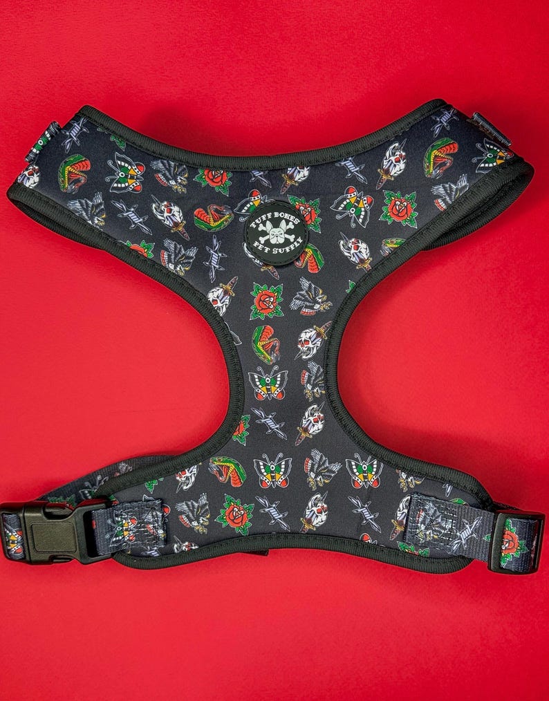 May include: Black dog harness with a tattoo-inspired print featuring butterflies, roses, daggers, and skulls. The harness has a black adjustable buckle and the text "PUFF BONES PET SUPPLY" in a circle.
