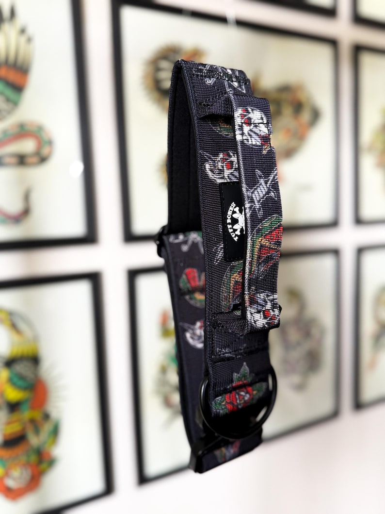 May include: A black nylon dog collar featuring a repeating pattern of skulls, roses, and barbed wire. The collar includes a black metal D-ring, a heavy-duty buckle, and a black fabric tag with the white text TUFF BONES and a skull logo.